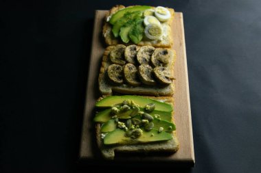 Tahtada üç sandviç, mantarlı sandviç, avokado ve tohumlar, avokado ve yumurtalı.