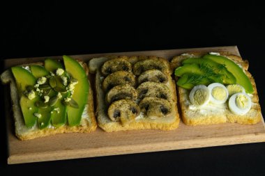 Tahtada üç sandviç, mantarlı sandviç, avokado ve tohumlar, avokado ve yumurtalı.