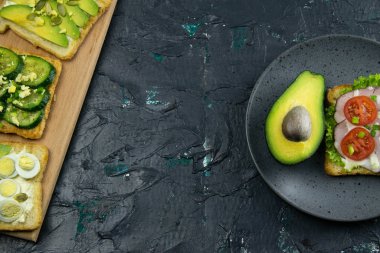 Jambonlu sandviç ve avokadolu gri tabakta domates.