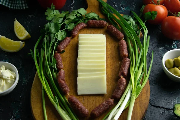 Mozzarella en rodajas en una tabla de madera, alrededor del jamón, cebollas verdes, tomate, souce, aceitunas, limón, especias, eneldo . — Foto de Stock