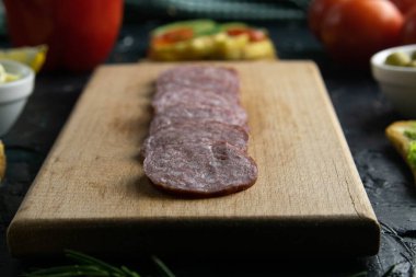 Tahtada dilimlenmiş salam, zeytin tahtasında diğer sandviçler, domates, limon ve sosla birlikte..