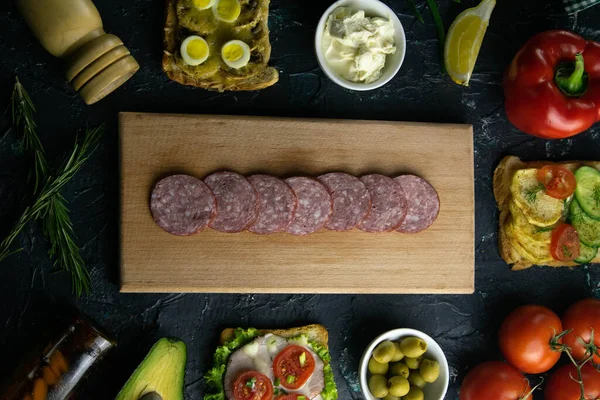 Skiveskåret salami på et træbræt, rundt om oliven bord med andre sandwich, tomat, citron og sauce . - Stock-foto