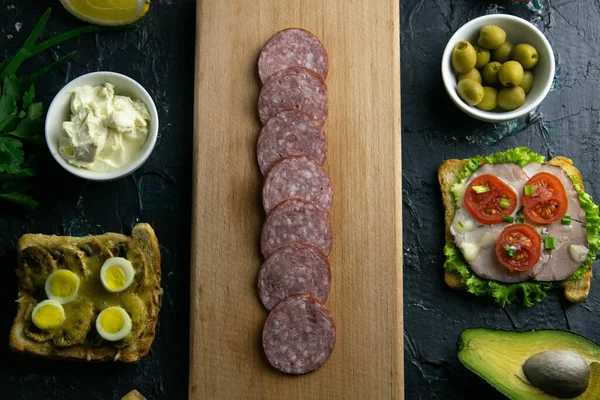Skiveskåret salami på et træbræt, rundt om oliven bord med andre sandwich, tomat, citron og sauce . - Stock-foto
