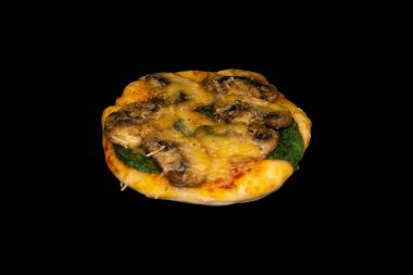 Siyah arka planda ıspanaklı, mantarlı ve peynirli küçük bir pizza.