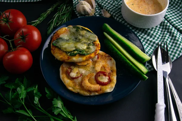 Pequeña mini pizza con camarones y queso en plato azul con pepino alrededor de un plato de tomates, salsa, hierbas y cubiertos —  Fotos de Stock