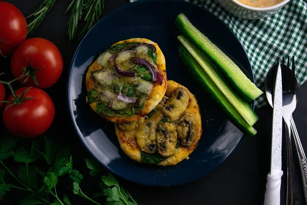 Small mini pizza with shrimp and cheese on blue plate with cucumber around a plate of tomatoes, sauce, herbs and cutlery — Stock Photo, Image