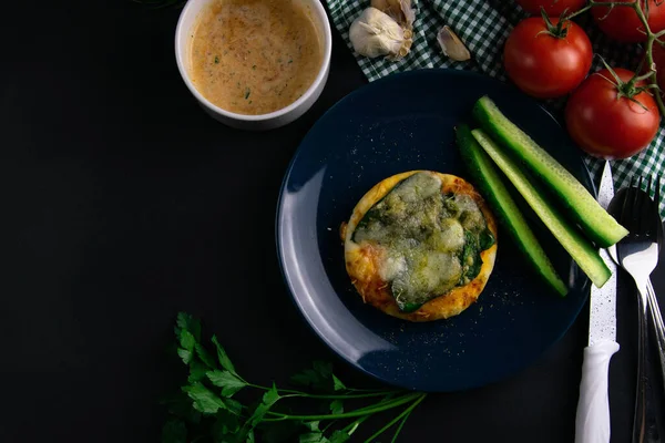 stock image Small mini pizza with spinach and cheese on blue plate with cucumber around a plate of tomatoes, sauce, herbs and cutlery