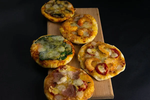 Pequeña mini pizza. Set de diferentes mini pizzas. Pizza sobre tabla de madera: con camarones, con champiñones, con espinacas y cebollas, con tocino, con paperoni, con tomates —  Fotos de Stock