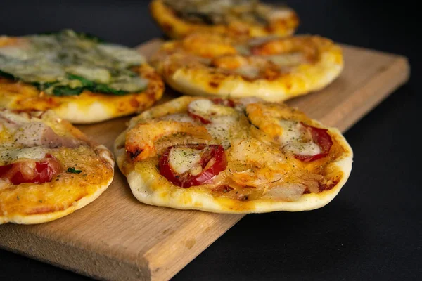 Маленька міні піца. Набір різних міні-піц. Піца на дерев'яній дошці: з креветками, з грибами, зі шпинатом і цибулею, з беконом, з папером, з помідорами — стокове фото