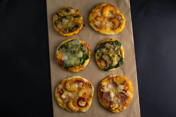 Küçük mini pizza. Farklı mini pizzalar. Kağıt üzerinde pizza: karidesli, mantarlı, ıspanaklı, soğanlı, pastırmalı, kağıtlı, domatesli. — Stok fotoğraf