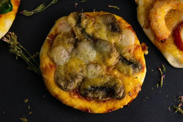 Маленька міні піца. Піца з грибами та сиром на чорному тлі. Поруч видно шматочки інших піц . — стокове фото