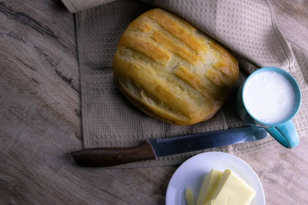 Ein Laib Brot unter einem Handtuch auf dem Tisch mit einem Glas Milch und Butter — Stockfoto