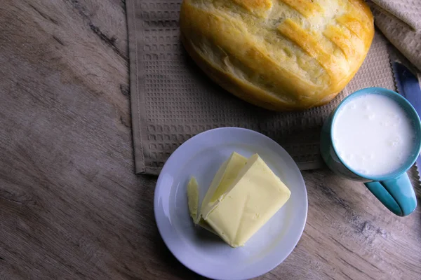 Ein Laib Brot unter einem Handtuch auf dem Tisch mit einem Glas Milch und Butter — Stockfoto