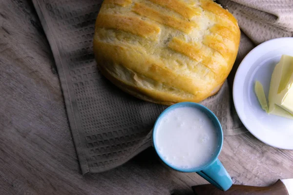 Bochník chleba pod ručníkem na stole se sklenicí mléka a másla — Stock fotografie