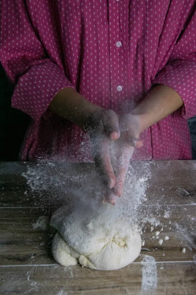 A woman claps her hands around the go splashes of flour. Process of preparation of dough for baking bread