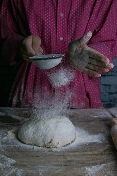 The woman sprinkles flour dough from the fullness for sifting flour, flour falls on the dough, a beautiful scattering of flour. Prepare to make bread and pastries. — Stock Photo, Image