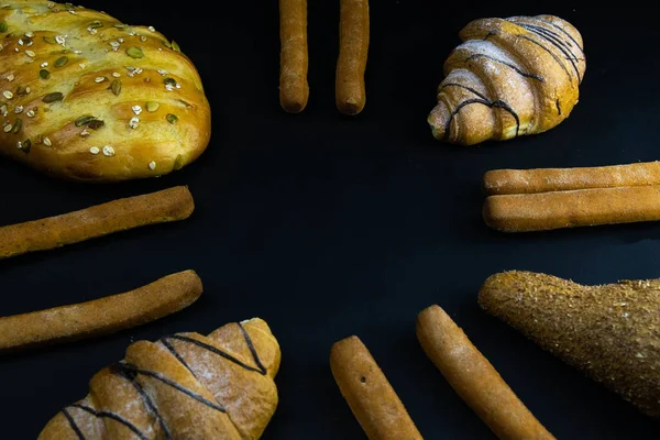 Diferentes tipos de pan fresco con grano sobre un fondo rústico negro. el pan está alrededor —  Fotos de Stock