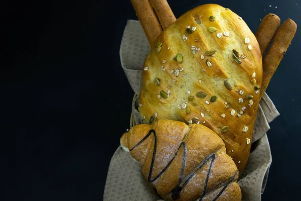 Különböző típusú friss kenyér gabonával fekete rusztikus háttérrel. — Stock Fotó