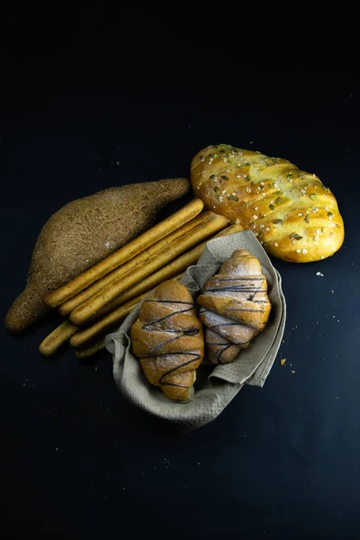 不同种类的新鲜羊角面包和面包，背景是黑色的. — 图库照片