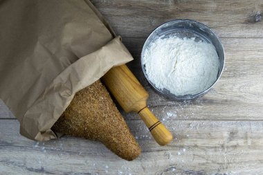 Hamur için sallanan bir somun ekmek ve yanında un bulunan ahşap bir masanın üstünde duran bir el işi çanta. Üst Görünüm