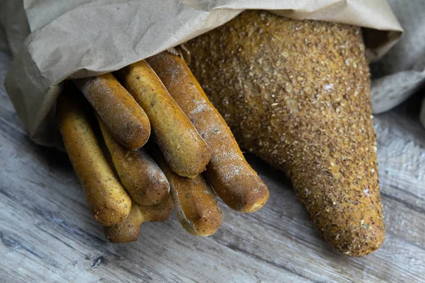 Diversi tipi di pane fresco in una borsa artigianale poggiano su un tavolo di legno . — Foto Stock