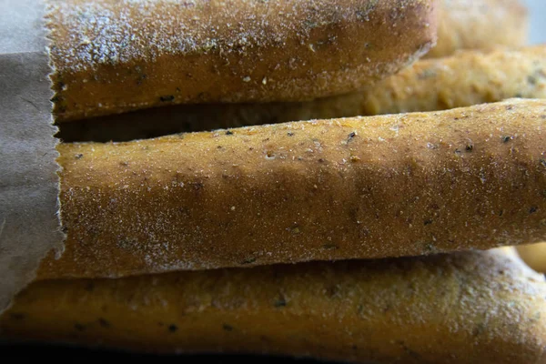 Different types of fresh spice bread sticks in a craft bag stand on a wooden table.