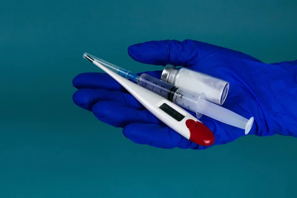Lékařská ruka v modré rukavici drží teploměr injekční stříkačku a koronavirovou vakcínu — Stock fotografie