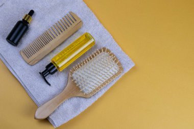 Kozmetik ürünleri, kokoba, argan ya da hindistan cevizi yağı. Turuncu arka planda duran havlunun üzerindeki yağ şişeleri ve taraklar.