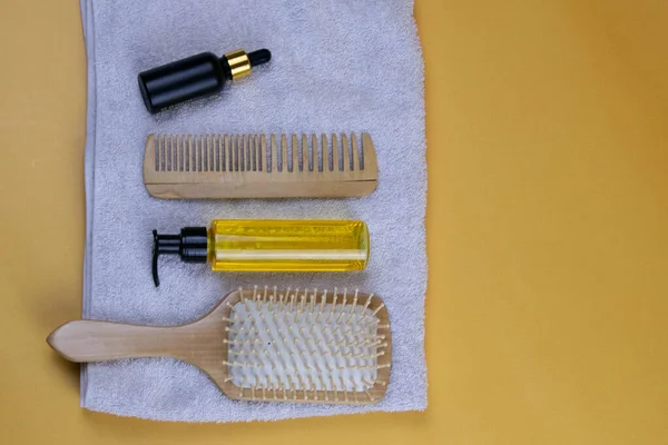 Cosmetics for hair care with jojoba, argan or coconut oil. Oil bottles and combs on a towel that stands on an orange background.