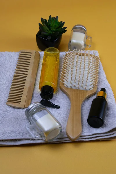 Cosmetics for hair care with jojoba, argan or coconut oil. Oil bottles and combs on a towel that stands on an orange background.