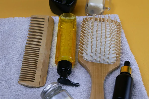Cosmetics for hair care with jojoba, argan or coconut oil. Oil bottles and combs on a towel that stands on an orange background.