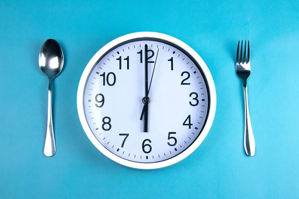 Ένα ρολόι δείχνει ακριβώς 6 ώρες, δίπλα σε ένα πιρούνι και ένα κουτάλι είναι σε μπλε φόντο. — Φωτογραφία Αρχείου