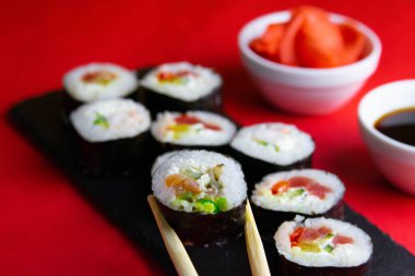 Çubuklar granit bir tahta rulo içinde rulo, yanında zencefil ve soya sosu, her şey kırmızı arka planda duruyor.