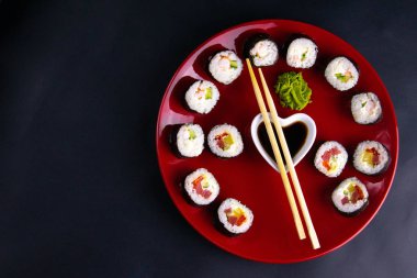 Soya sosu, wasabi ve suşi çubuklarıyla birlikte kırmızı bir tabağa konur. Tabak siyah bir arka planda durur.