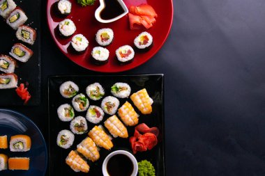 Soya sosu, wasabi ve suşi çubuklarıyla birlikte farklı tabaklara konur. Tabaklar siyah bir arkaplanda durur.