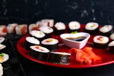 Soya sosu, wasabi ve suşi çubuklarıyla birlikte farklı tabaklara konur. Tabaklar siyah bir arkaplanda durur.