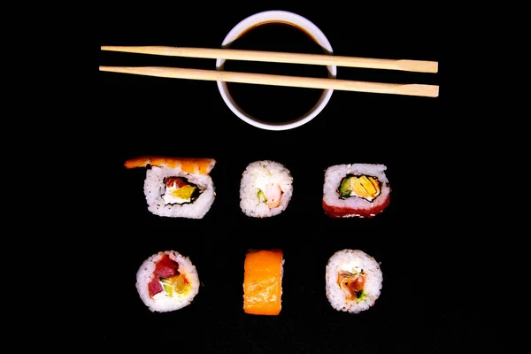 Eine Reihe von verschiedenen Rollen mit Sojasauce und Sushi-Sticks isoliert auf schwarzem Hintergrund — Stockfoto
