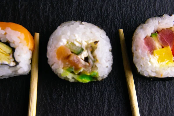 Kije trzymać rolki, które stoją na czarnej tablicy grafitowej do sushi, który stoi na czarnym tle i rolki na sushi spin — Zdjęcie stockowe