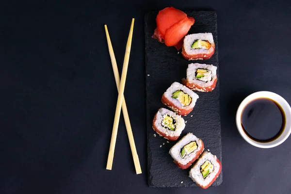 Rolki na granitowym stoisku na sushi układane są w formie smoka, obok stojaków na sushi i sos sojowy. — Zdjęcie stockowe