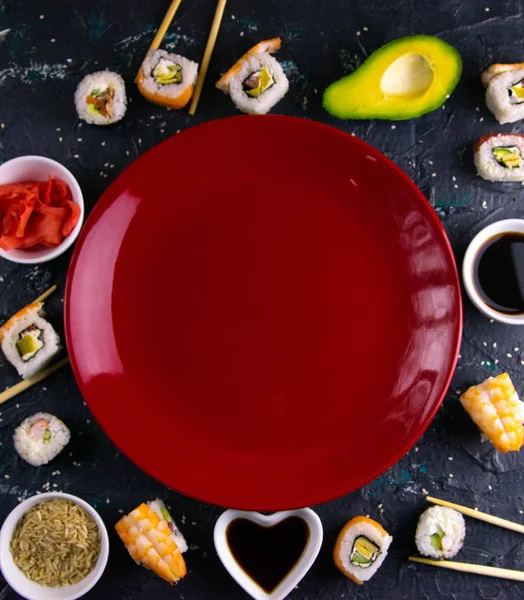 Different roles, avocado, red marinated ginger, rice, soy sauce are laid out on the perimeter in the shape of a square inside the free space.