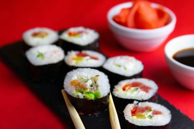 Çubuklar granit bir tahta rulo içinde rulo, yanında zencefil ve soya sosu, her şey kırmızı arka planda duruyor.