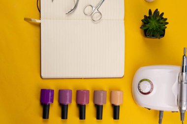 Set of cosmetic tools for manicure and pedicure on an orange background. Nearby there is an open notebook for writing, gel varnishes, a mill, nail files, scissors and nippers.
