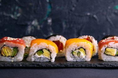 Siyah arka planda suşi için siyah granit bir tahtanın üzerinde farklı şekillerde rulo duruyor.