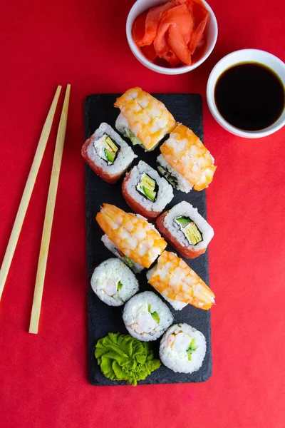 Płyta granitowa do sushi, wypełniona rolkami różnego rodzaju, obok stojaków do sushi, czerwonego marynatora i sosu sojowego. — Zdjęcie stockowe