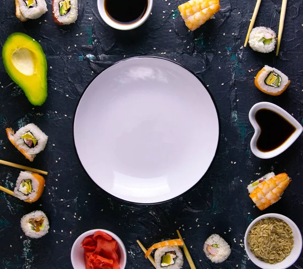 Different roles, avocado, red marinated ginger, rice, soy sauce are laid out on the perimeter in the shape of a square inside the free space.
