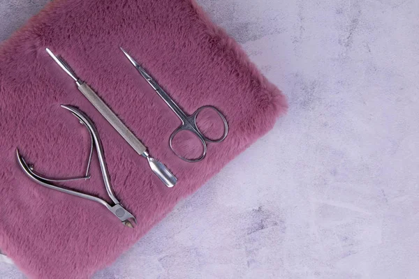 A set of cosmetic tools for manicure and pedicure stand on a pink fluffy notebook for recording clients. tweezers, scissors and tongs.