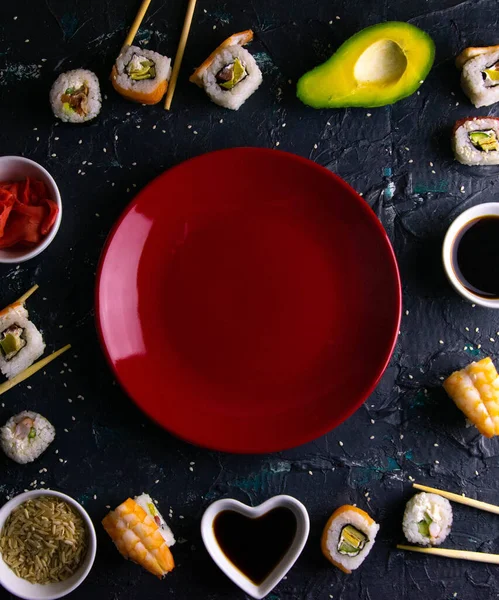 Different roles, avocado, red marinated ginger, rice, soy sauce are laid out on the perimeter in the shape of a square inside the free space.