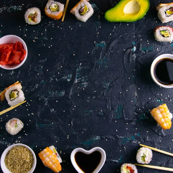 Different roles, avocado, red marinated ginger, rice, soy sauce are laid out on the perimeter in the shape of a square inside the free space.