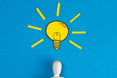 Kafasında mavi bir arka planda sarı el işi kağıt olan ampulü olan bir adamın ahşap biblosu..