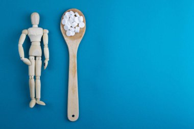 Wooden toy figure with pills on blue background. Various capsules, tablets and medicine on blue pastel trendy background. Pills concept.
